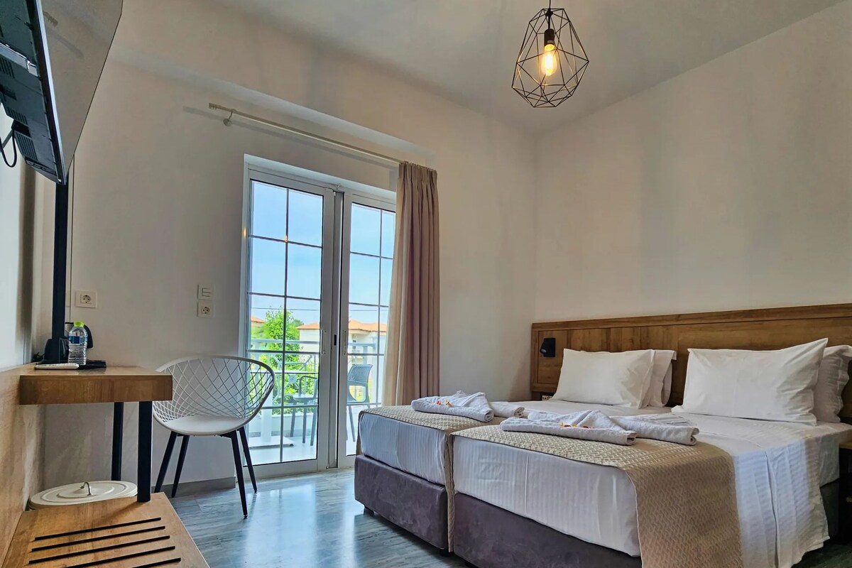 A hotel room with a bed, a desk, a chair, and a view through a large window.