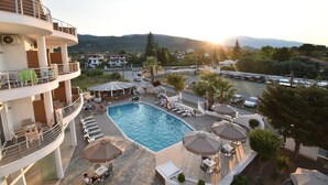 A pool area with lounge chairs and umbrellas, a multi-level building with balconies, and a view of the surrounding landscape. - Olympion Melathron (Dio-Olympos)