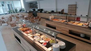 A buffet area with various food options, a seating area with chairs, and a kitchen in the background. - Olympion Melathron (Dio-Olympos)