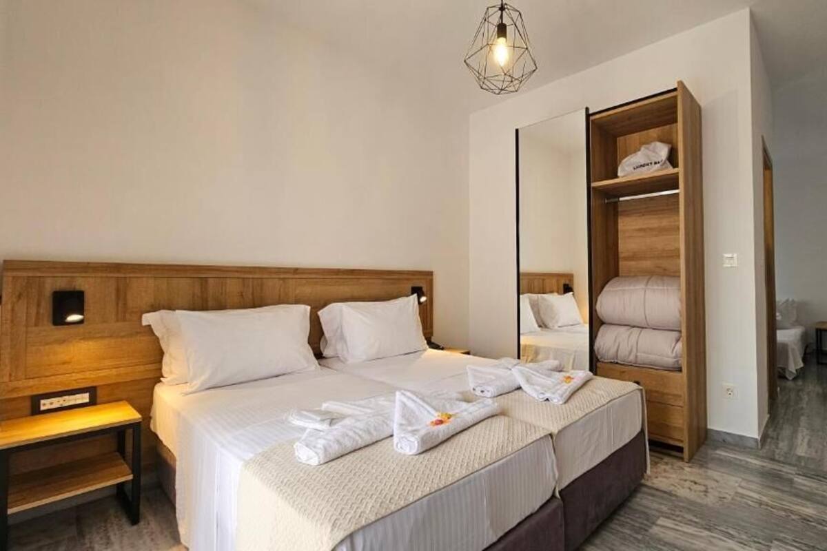 Habitación de hotel con una cama grande, cabecera de madera, mesita de noche, armario y espejo.