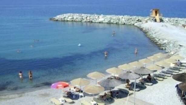 A beach with clear blue water, a rocky breakwater, and several umbrellas and lounge chairs. - Olympion Melathron (Dio-Olympos)