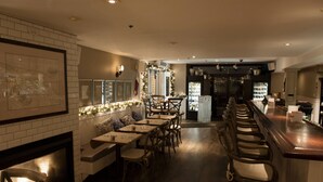 A restaurant with a long counter, wooden chairs, and a fireplace.