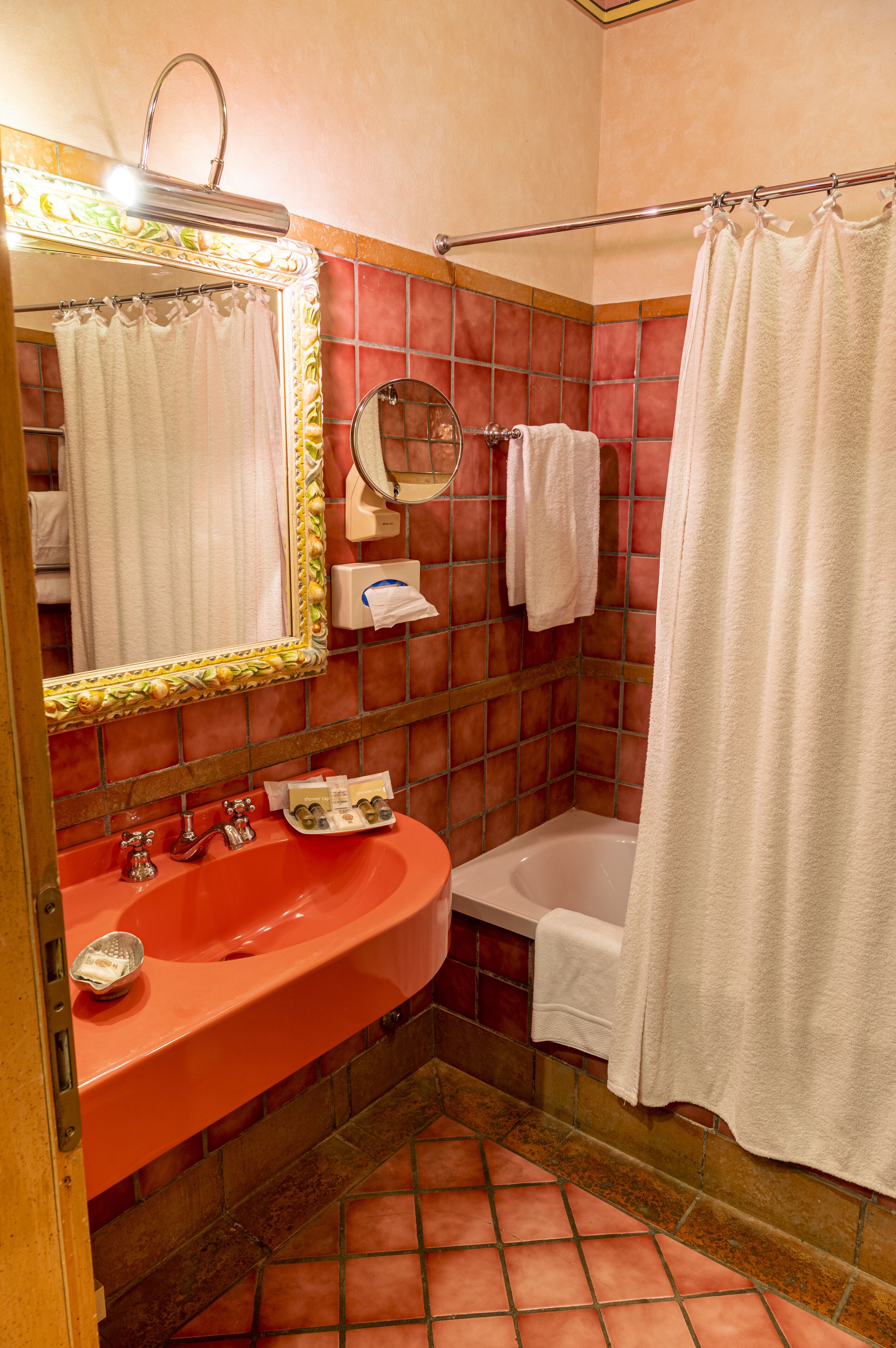 A bathroom with a red sink, a white bathtub, and a shower curtain.