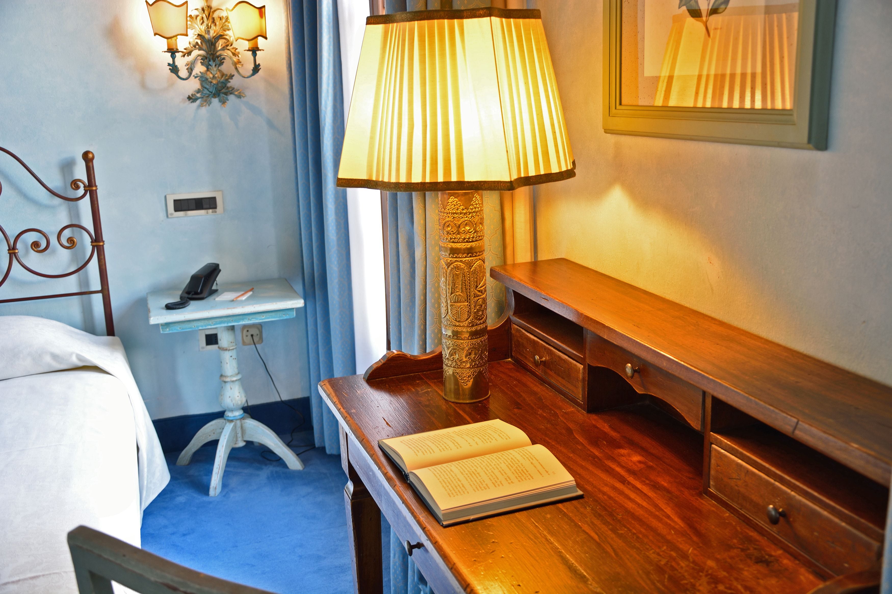 Una habitación de hotel con una cama, mesita de noche, lámpara y cómoda de madera.