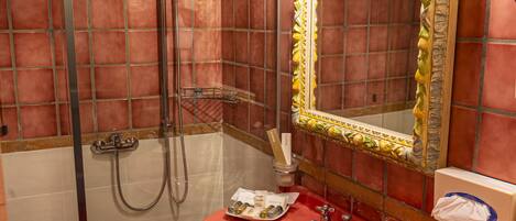 Un baño con ducha de vidrio, un lavamanos rojo y un espejo con marco decorativo.