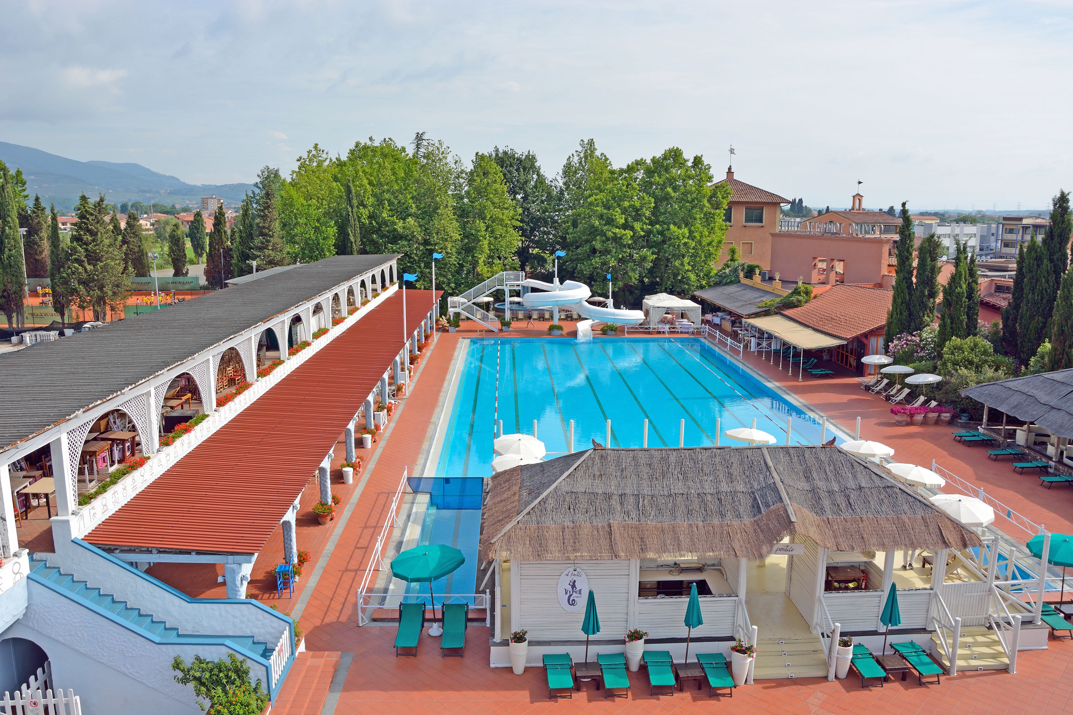 Uma piscina com um bangalô de colmo, espreguiçadeiras e uma área de estar coberta.