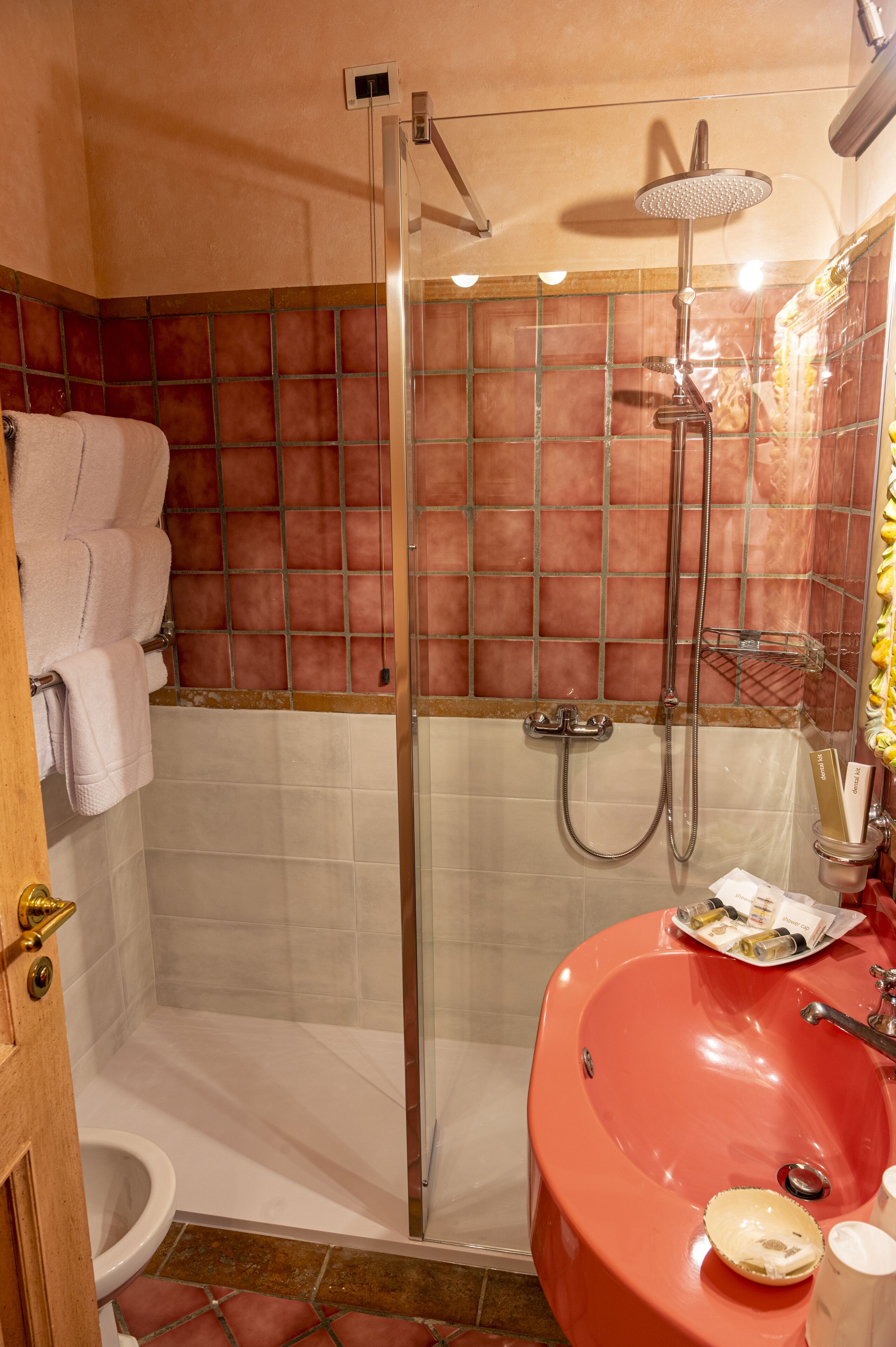 A bathroom with a glass-enclosed shower, a red sink, and a toilet.