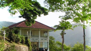 A two-story building with a balcony, a stone wall, and a car parked in front.
