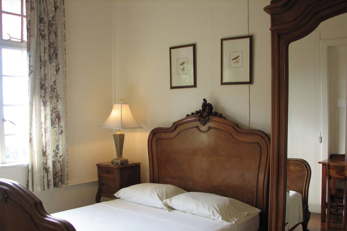 A neatly made bed with white linens, a wooden headboard, a bedside lamp, and two framed pictures on the wall.