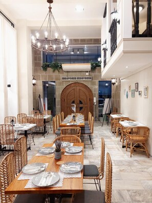 A spacious dining area with multiple tables and chairs, a large chandelier, and a stone fireplace. - The Southern Cross Hotel (Manila)