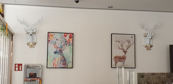 Una habitación con dos decoraciones de cabeza de ciervo, un cuadro colorido y un retrato enmarco de un ciervo.