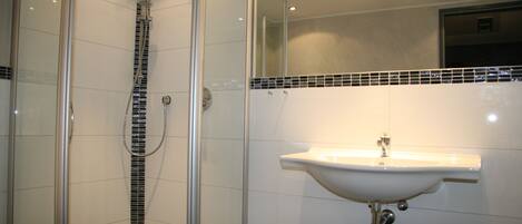 Un baño moderno con ducha de vidrio, lavamanos blanco y salpicadero de azulejos.