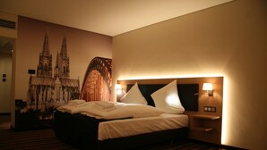 Une chambre d’hôtel dotée d’un grand lit, d’une tête de lit avec éclairage intégré, d’une table de chevet et d’une fresque murale représentant une cathédrale.