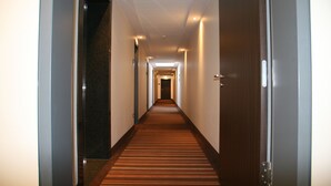 Un couloir d’hôtel avec un sol recouvert de moquette, des portes en bois et un plafond doté d’un éclairage encastré.