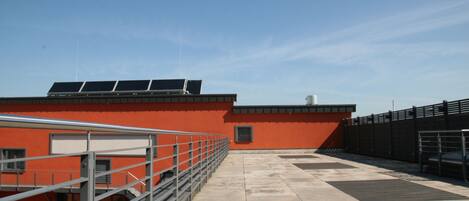 A rooftop terrace with solar panels, a metal railing, and a clear sky.