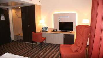 A hotel room with a bed, a desk with a computer, a TV, and two chairs.