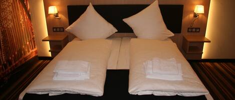 Cama doble con dos almohadas y dos mesitas de noche con lámparas.