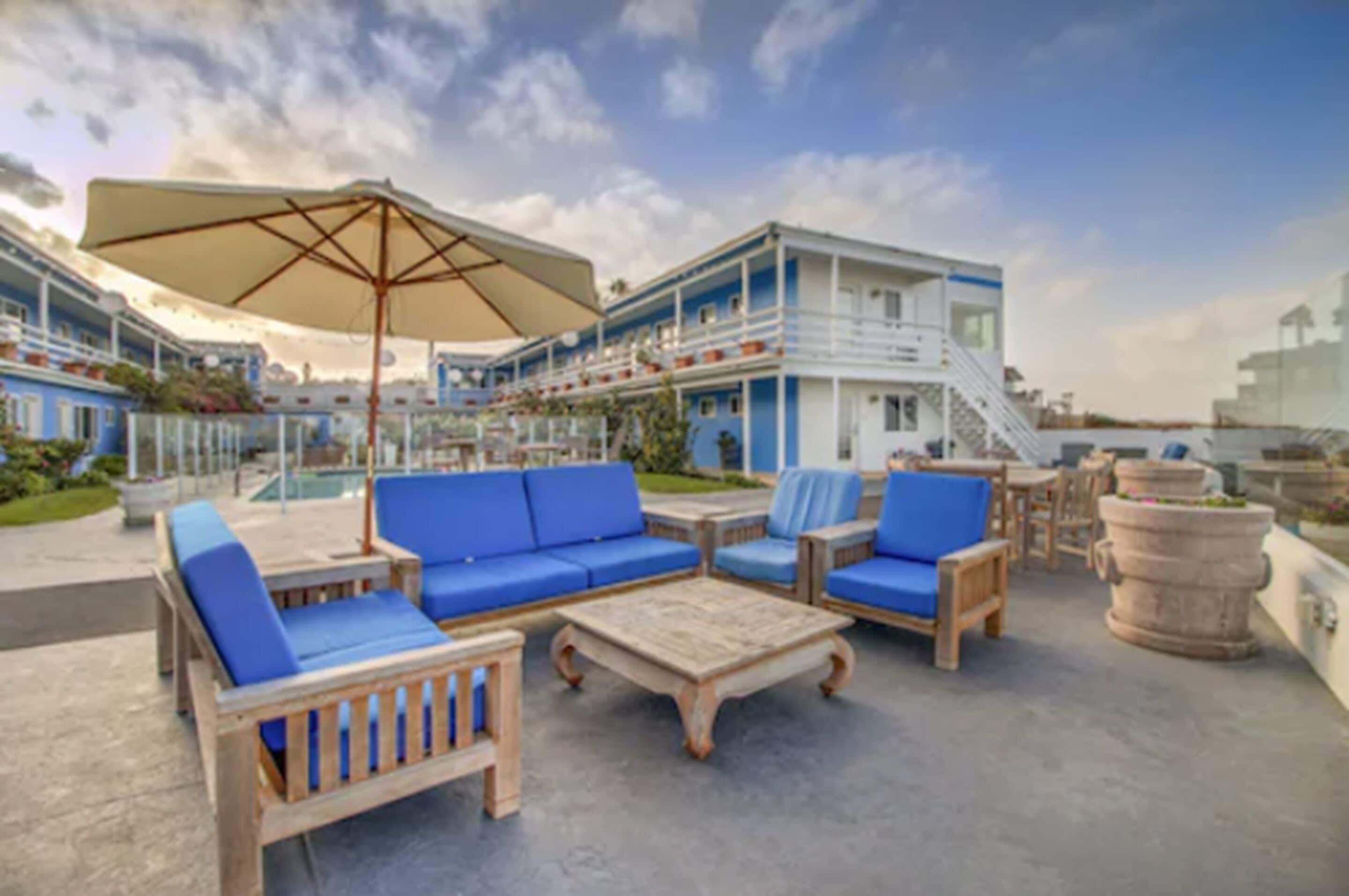 A rooftop lounge area with blue cushioned seating, a wooden coffee table, and a large umbrella.