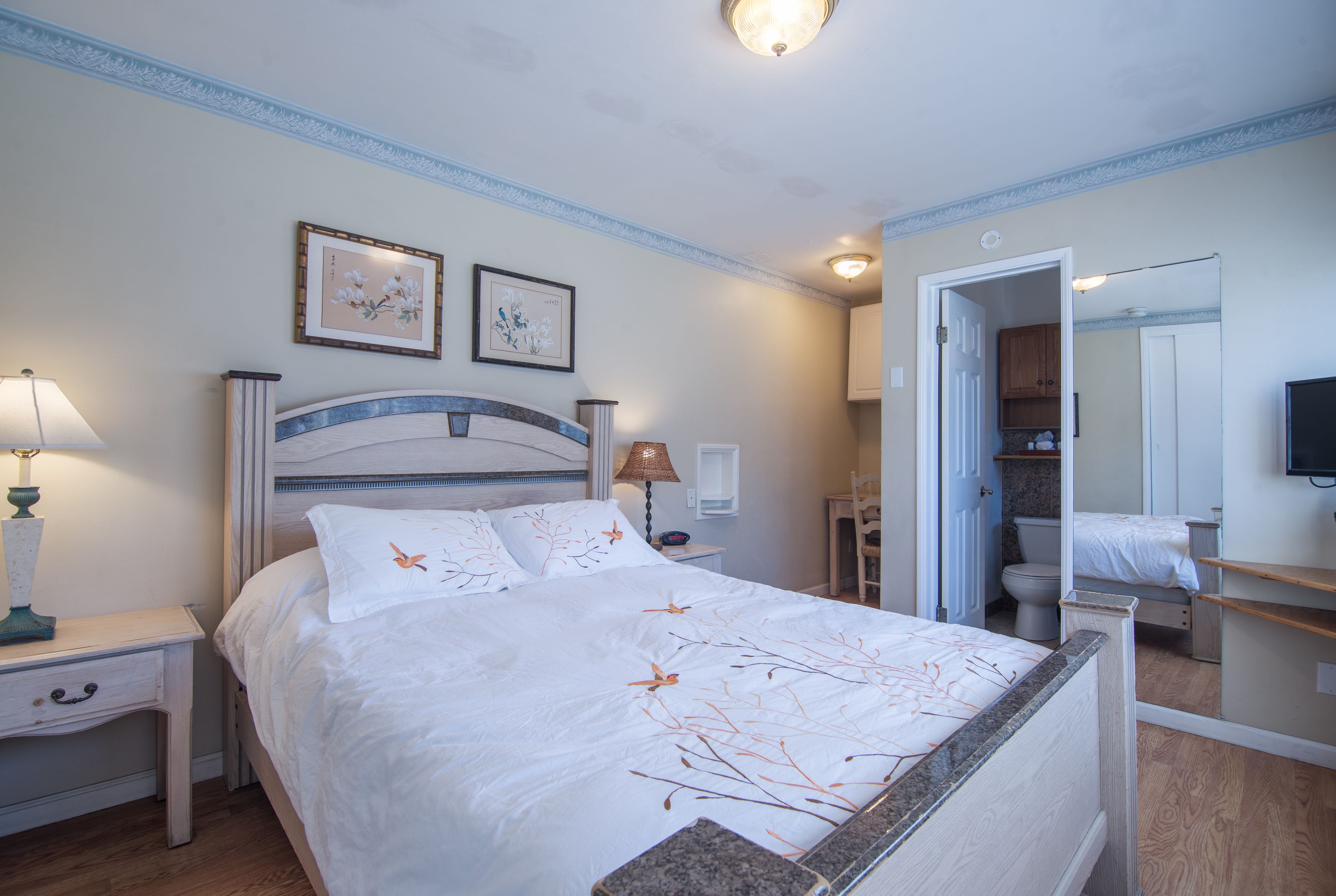 A bedroom with a bed, nightstands, a lamp, a mirror, and a bathroom visible through an open door.