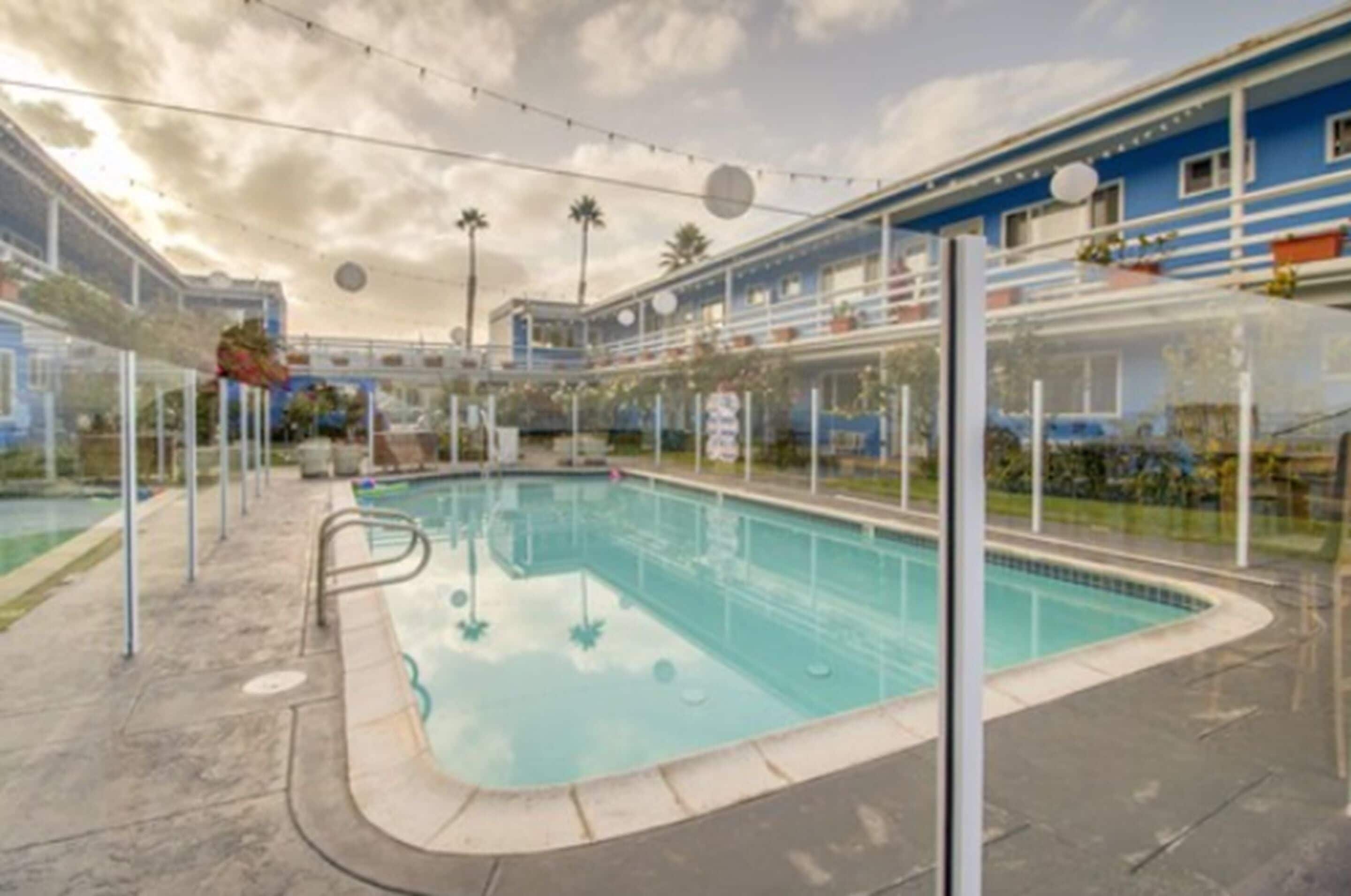 A swimming pool with a clear blue water, surrounded by a glass enclosure and a blue building with balconies.