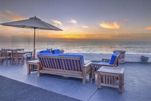 A beachside lounge with wooden furniture and a large umbrella, overlooking the ocean. - The Inn at Sunset Cliffs (San Diego)