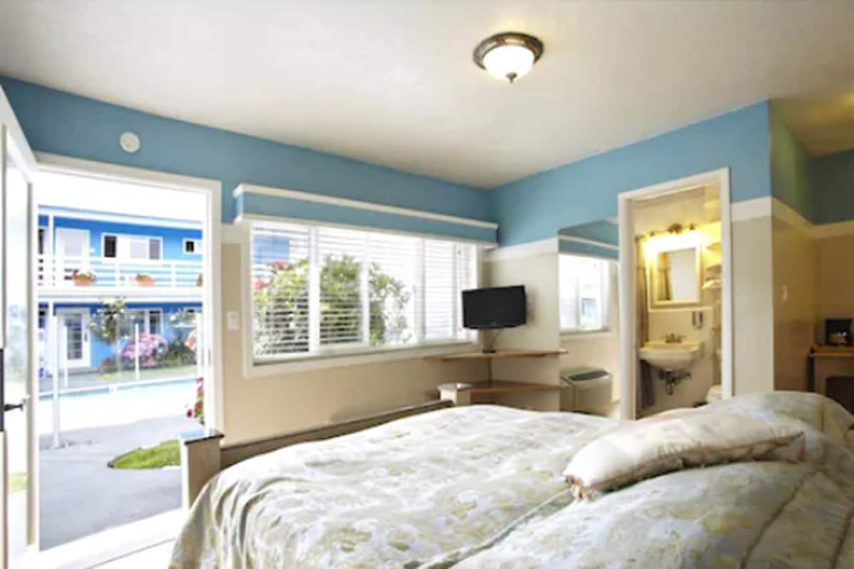 A bedroom with a bed, a television, a sink, and a window with blinds.