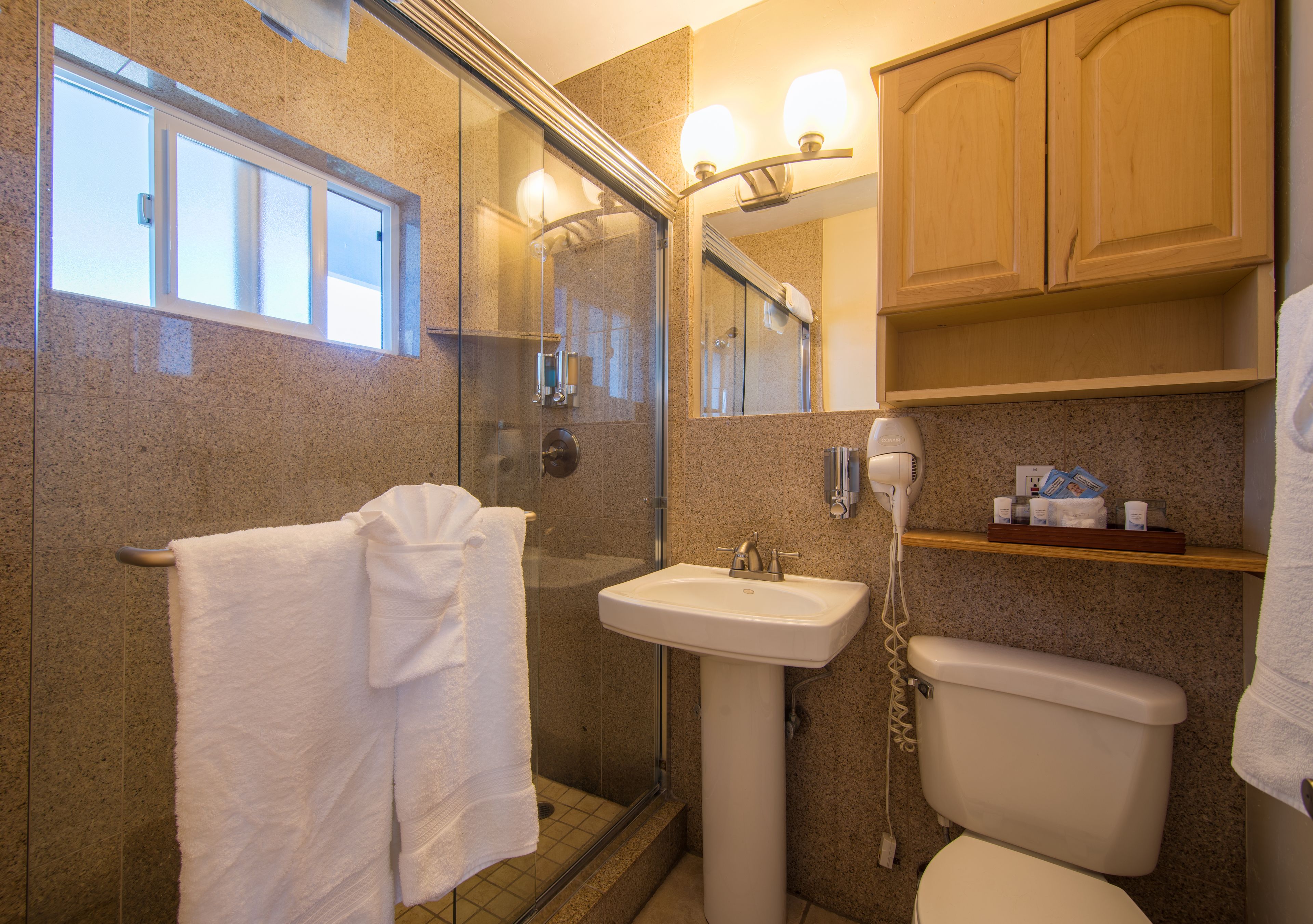 Un bagno con box doccia in vetro, lavabo, WC e mobili contenitori in legno.