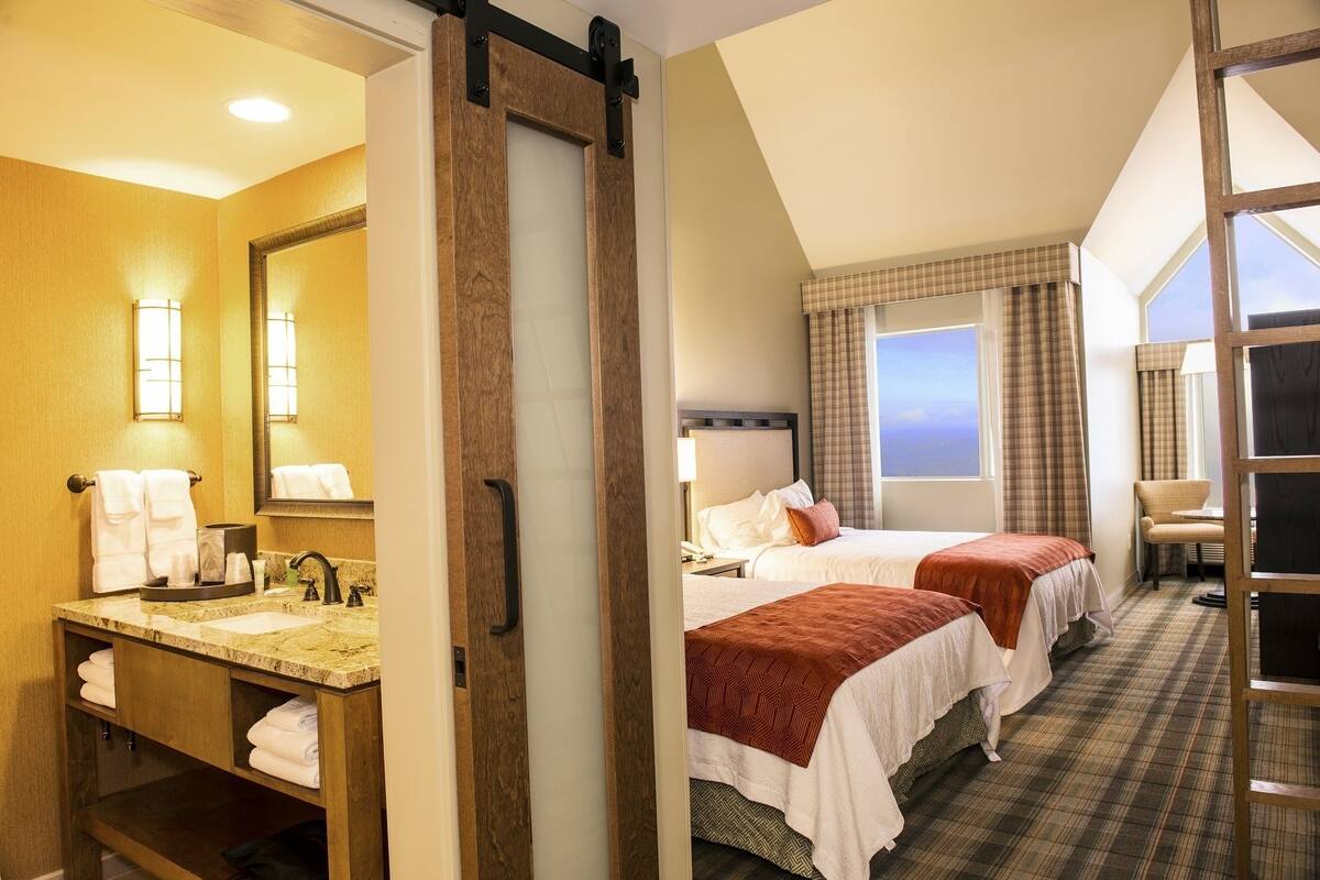 A hotel room with two beds, a bathroom with a vanity, and a view of the sky through the window.
