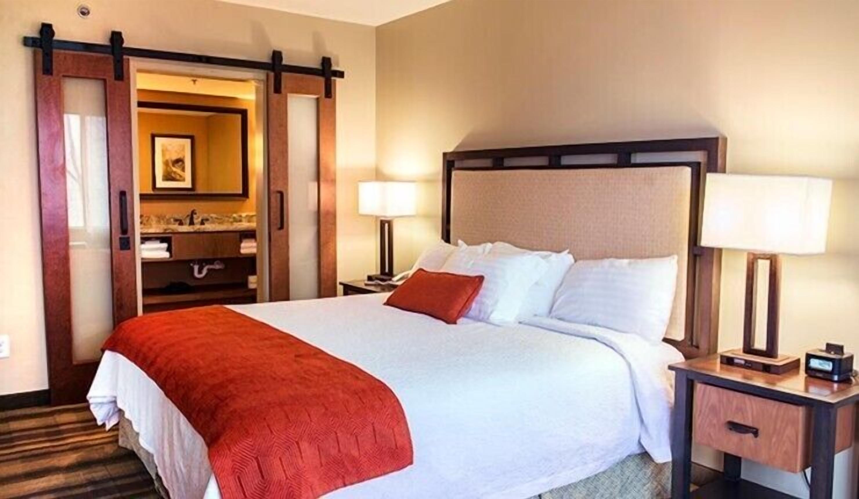 A hotel room with a large bed, two bedside tables with lamps, a wooden wardrobe, and a mirror.