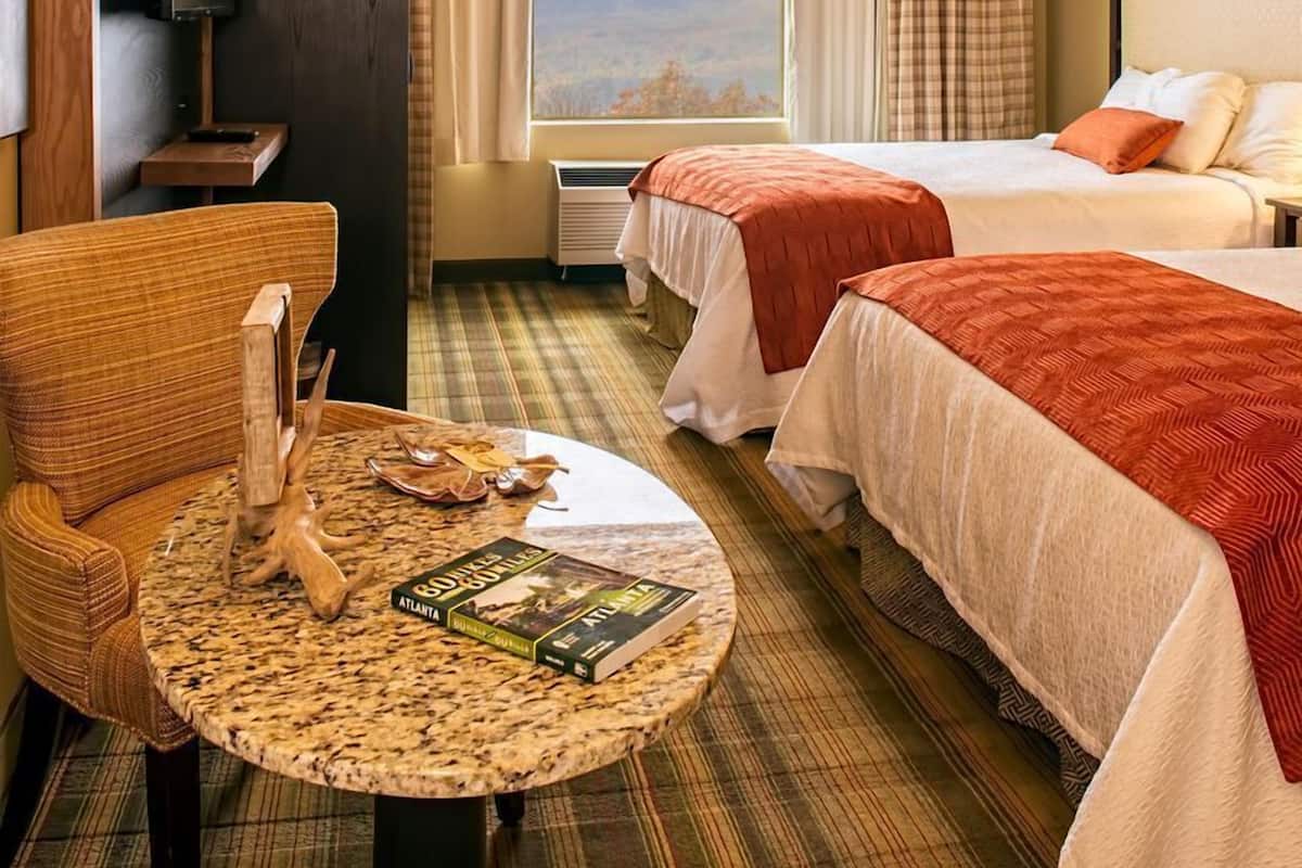 A hotel room with two beds, a television, a small table with books, and a window with a view.