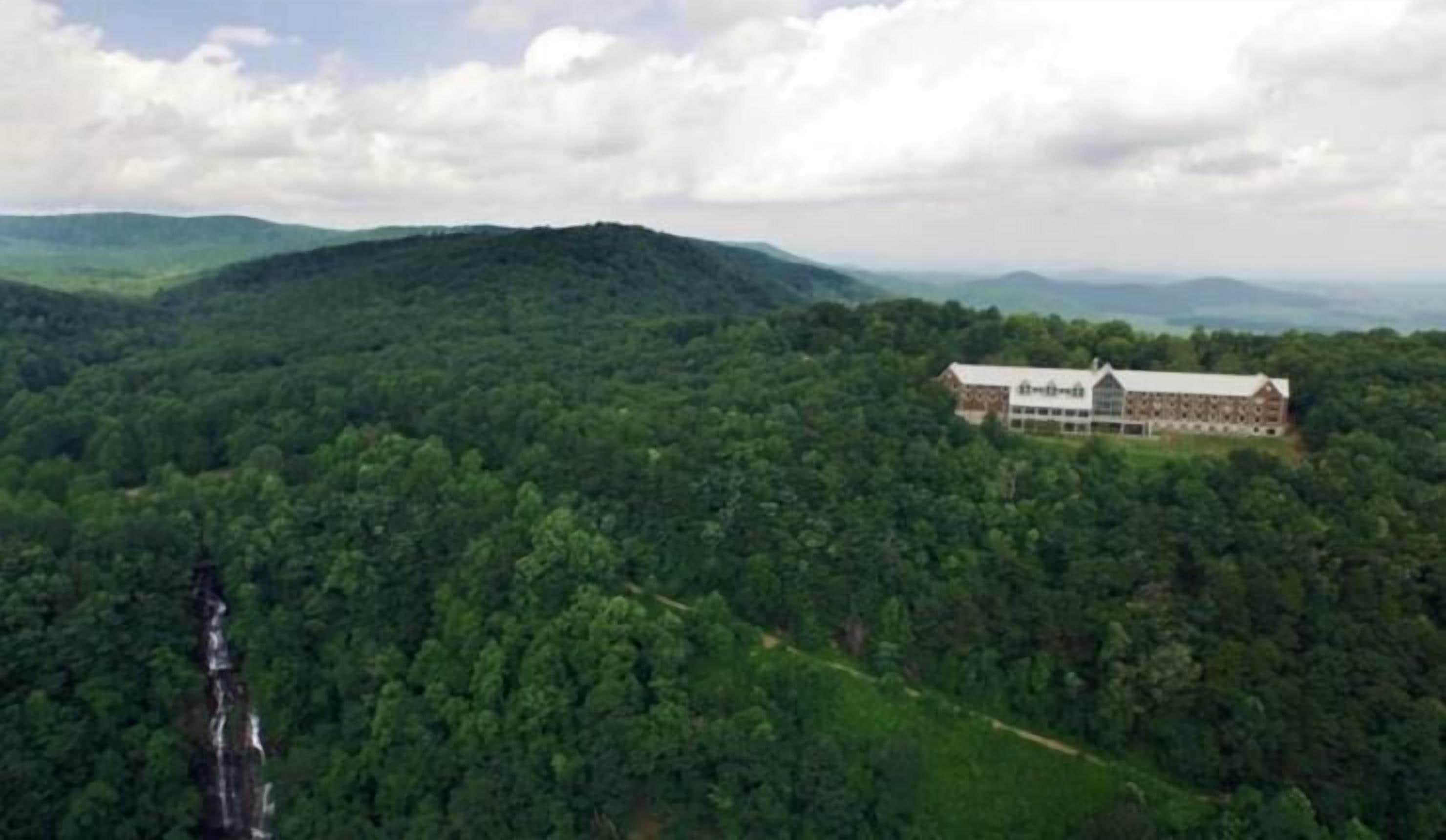 A large building with a long, horizontal structure, surrounded by dense forest and hills.