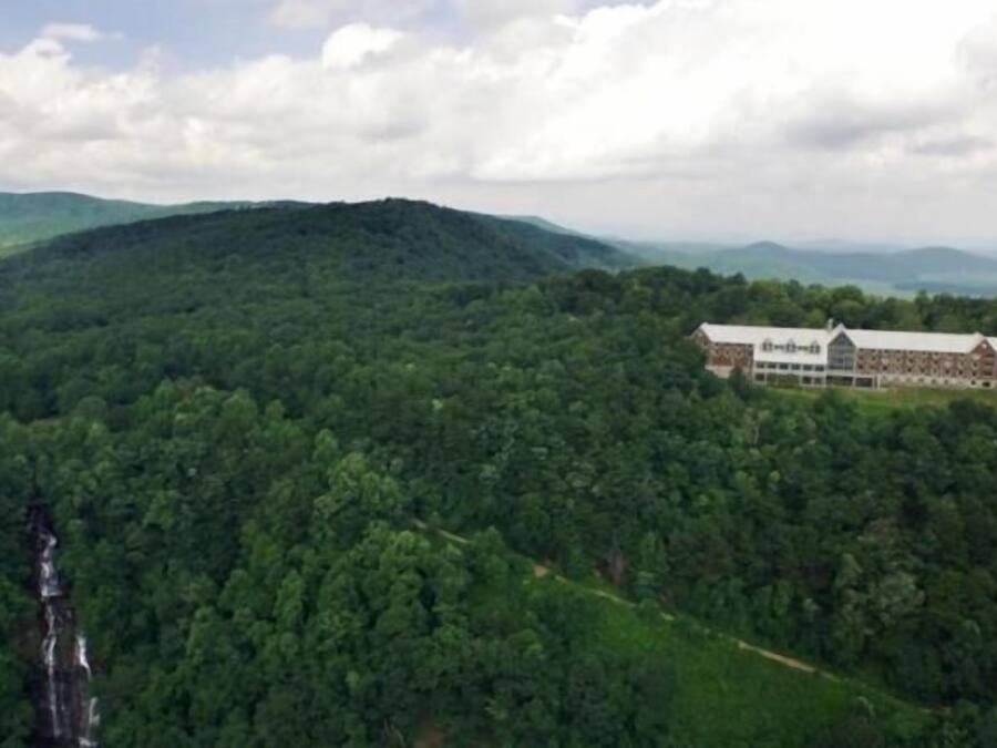 A large building with a long, horizontal structure, surrounded by dense forest and hills.