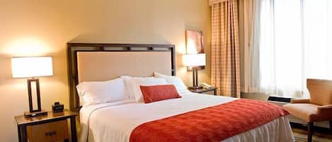 A hotel room with a bed, two bedside tables, a chair, and a window with curtains.