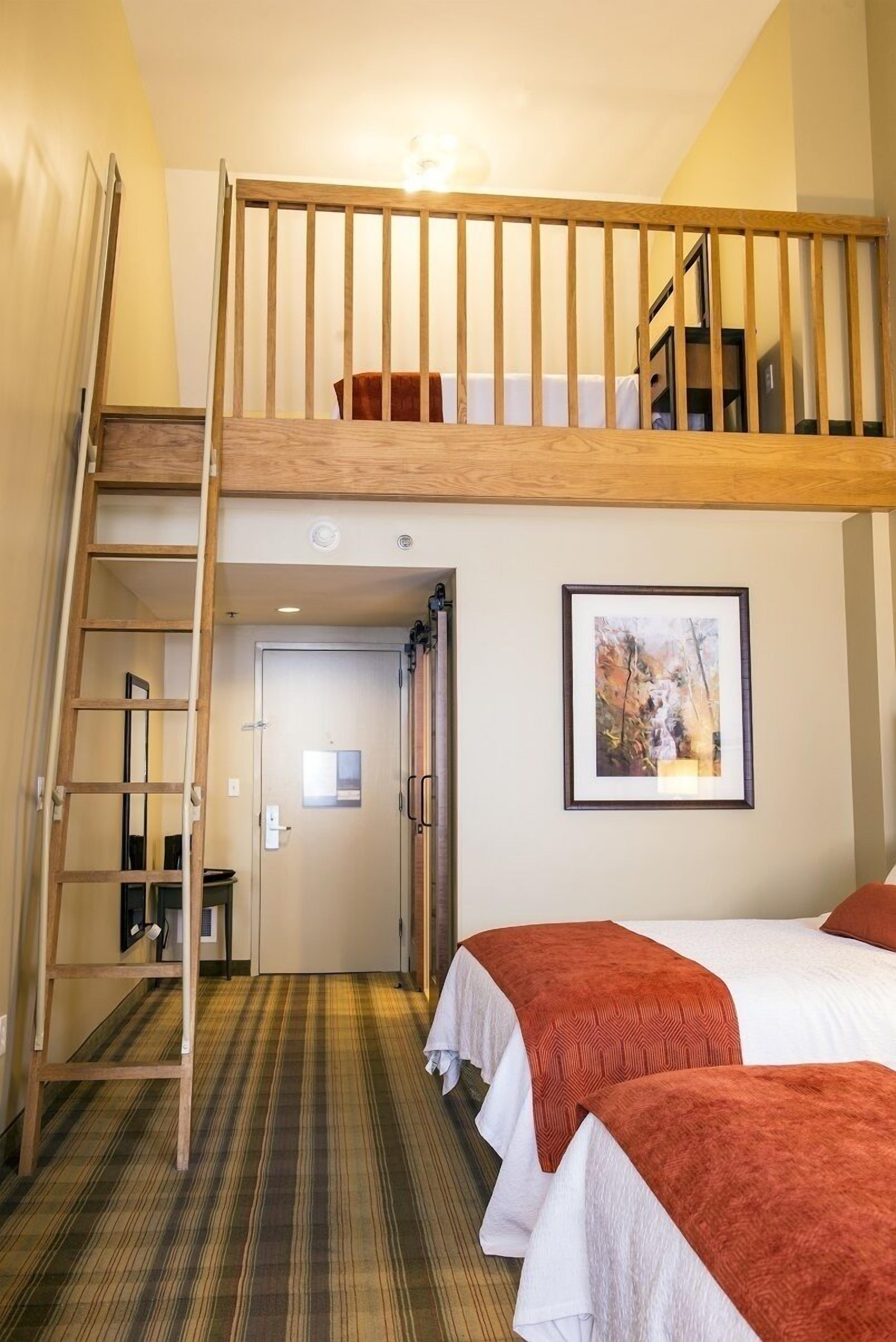 A room with a bunk bed, a ladder, a framed picture on the wall, and a door leading to another room.