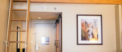 A room with a bunk bed, a ladder, a framed picture on the wall, and a door leading to another room.