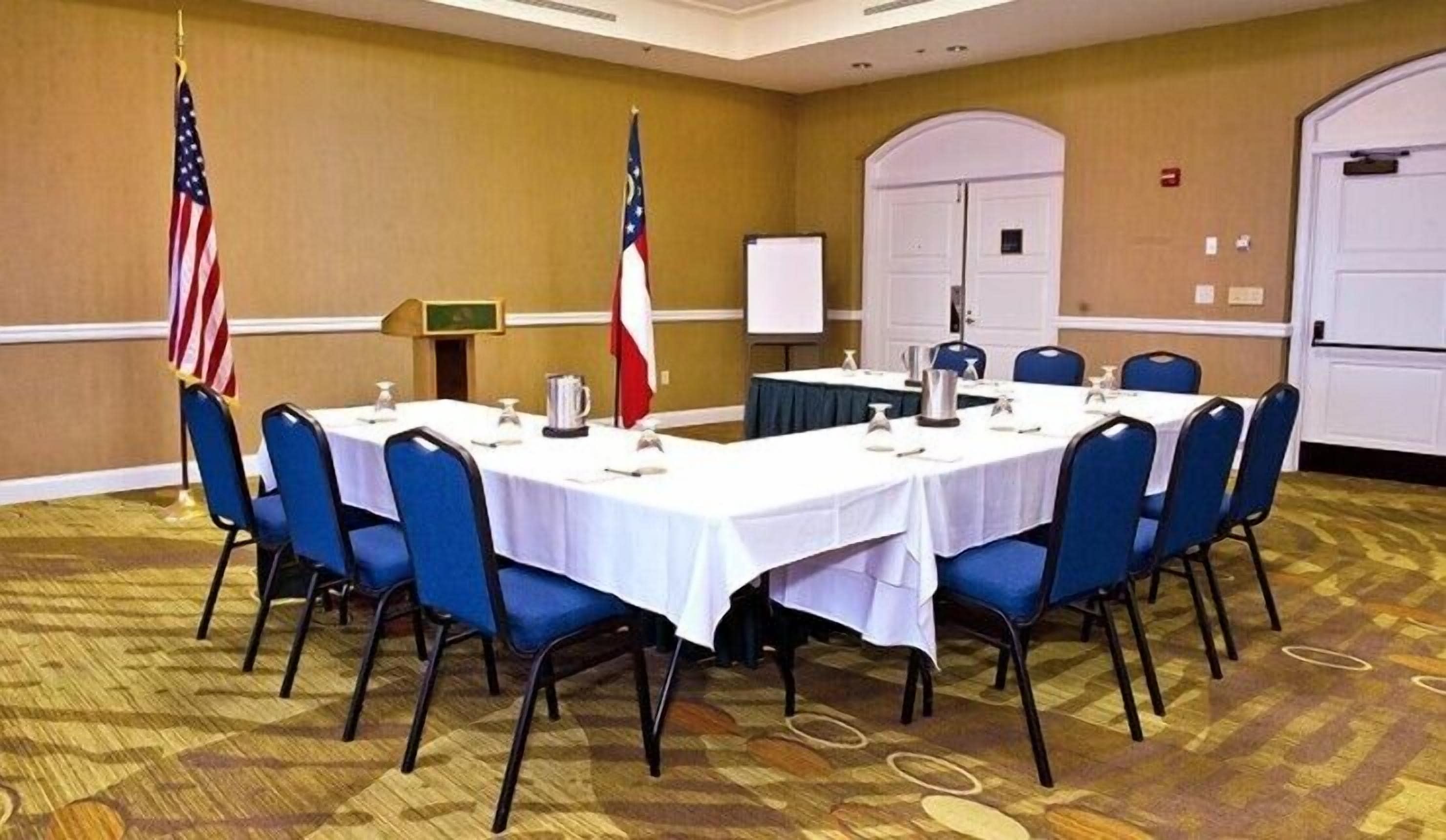 A conference room with a long table, blue chairs, and two flags.