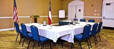 A conference room with a long table, blue chairs, and two flags.