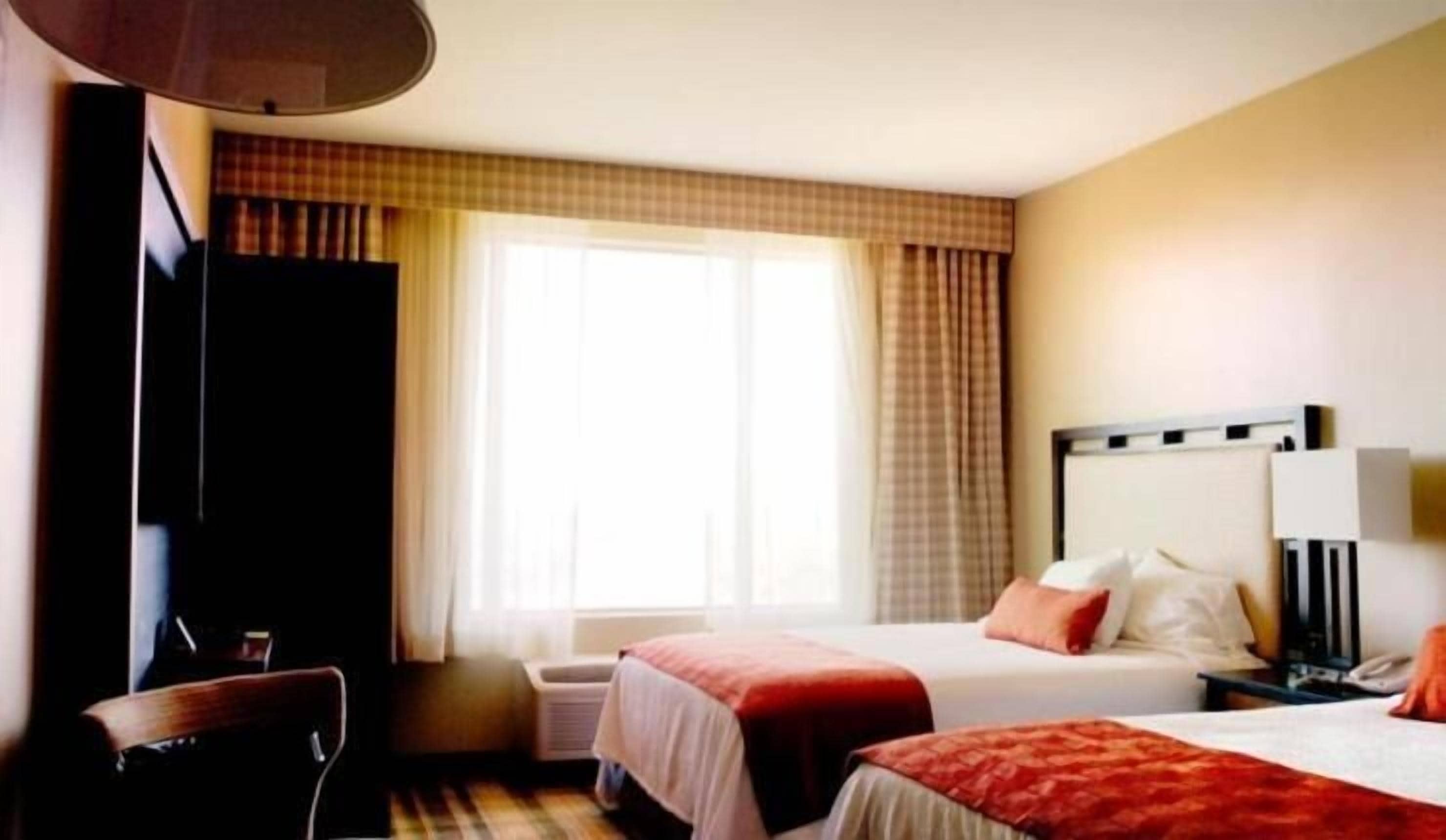 Camera d'albergo con due letti, una scrivania, una sedia, una televisione e un'ampia finestra con tende.