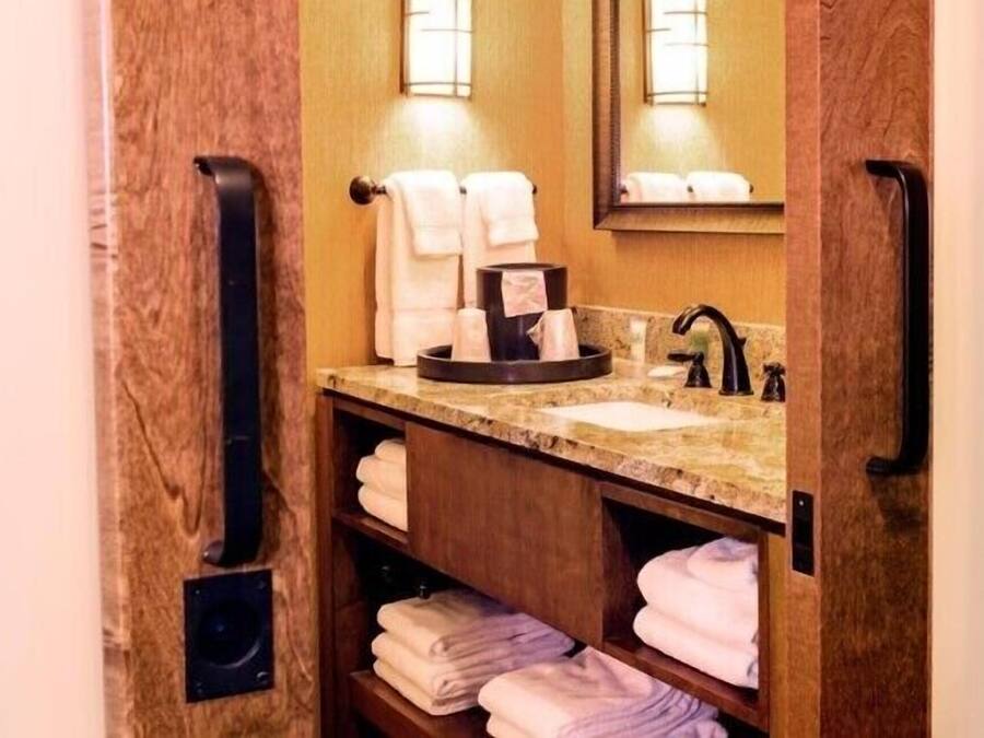 Un baño pequeño con encimera de mármol, un lavabo y un espejo. Hay toallas dobladas cuidadosamente en estantes y un toallero negro.