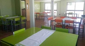 A dining area with green tables and chairs, large windows, and a tiled floor. - Juku Hostal (Calama)