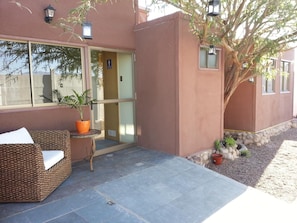 A building exterior with a glass door entrance, a potted plant, a wicker sofa, and a small table. - Juku Hostal (Calama)