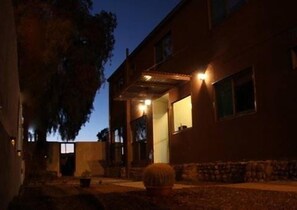 Un edificio con un patio cubierto, un árbol grande y un cactus en primer plano.