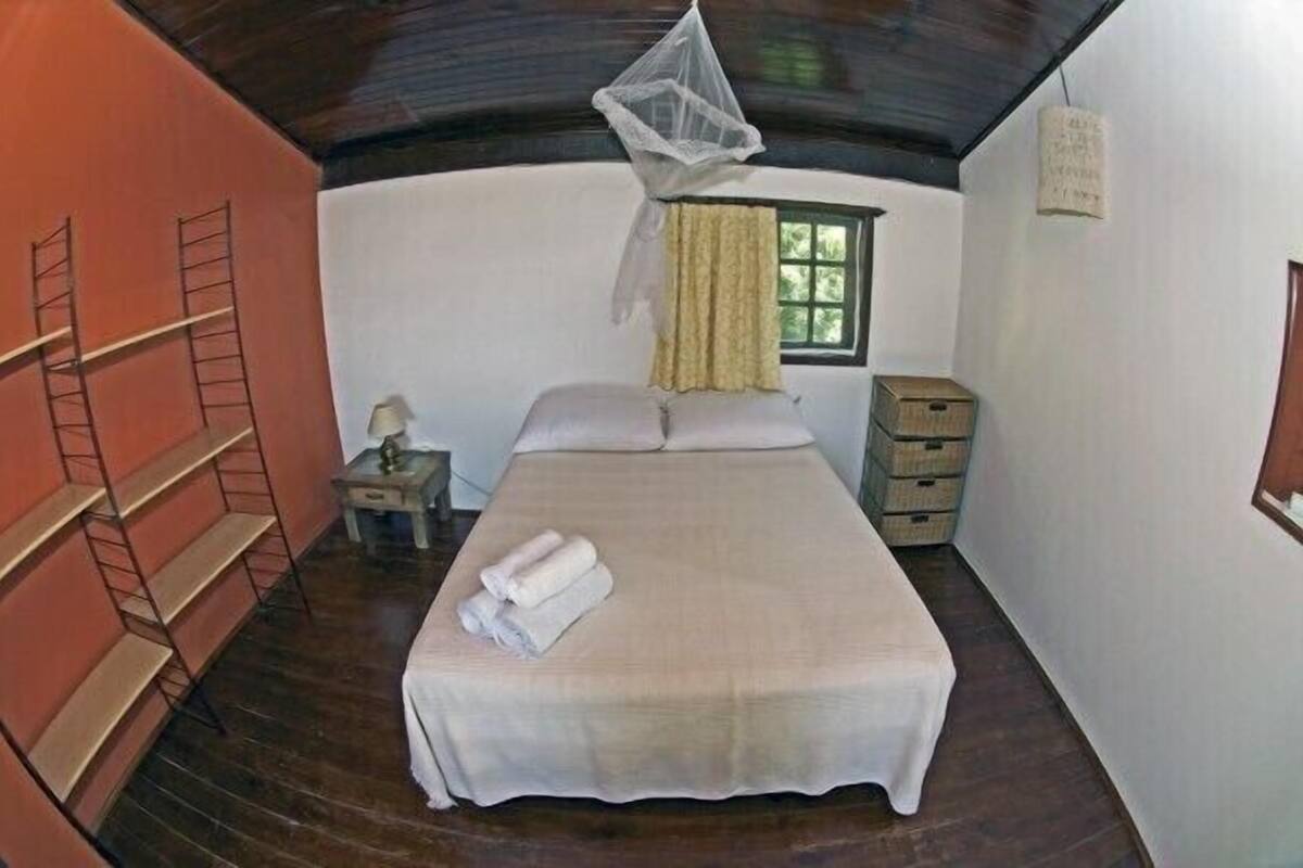 A bedroom with a bed, a nightstand, a window with curtains, a ladder, and a small cabinet.