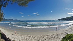 A beach with clear skies, waves, and people walking. - Pousada do Taxo (Garopaba)