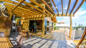 A wooden deck with outdoor furniture, a barbecue area, and a glass door leading to an interior space. - Pousada do Taxo (Garopaba)