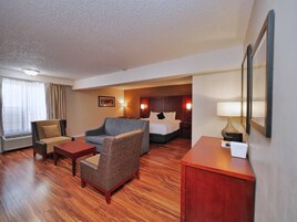 Una habitación de hotel con suelo de madera, una cama, un escritorio, una silla y un sofá.