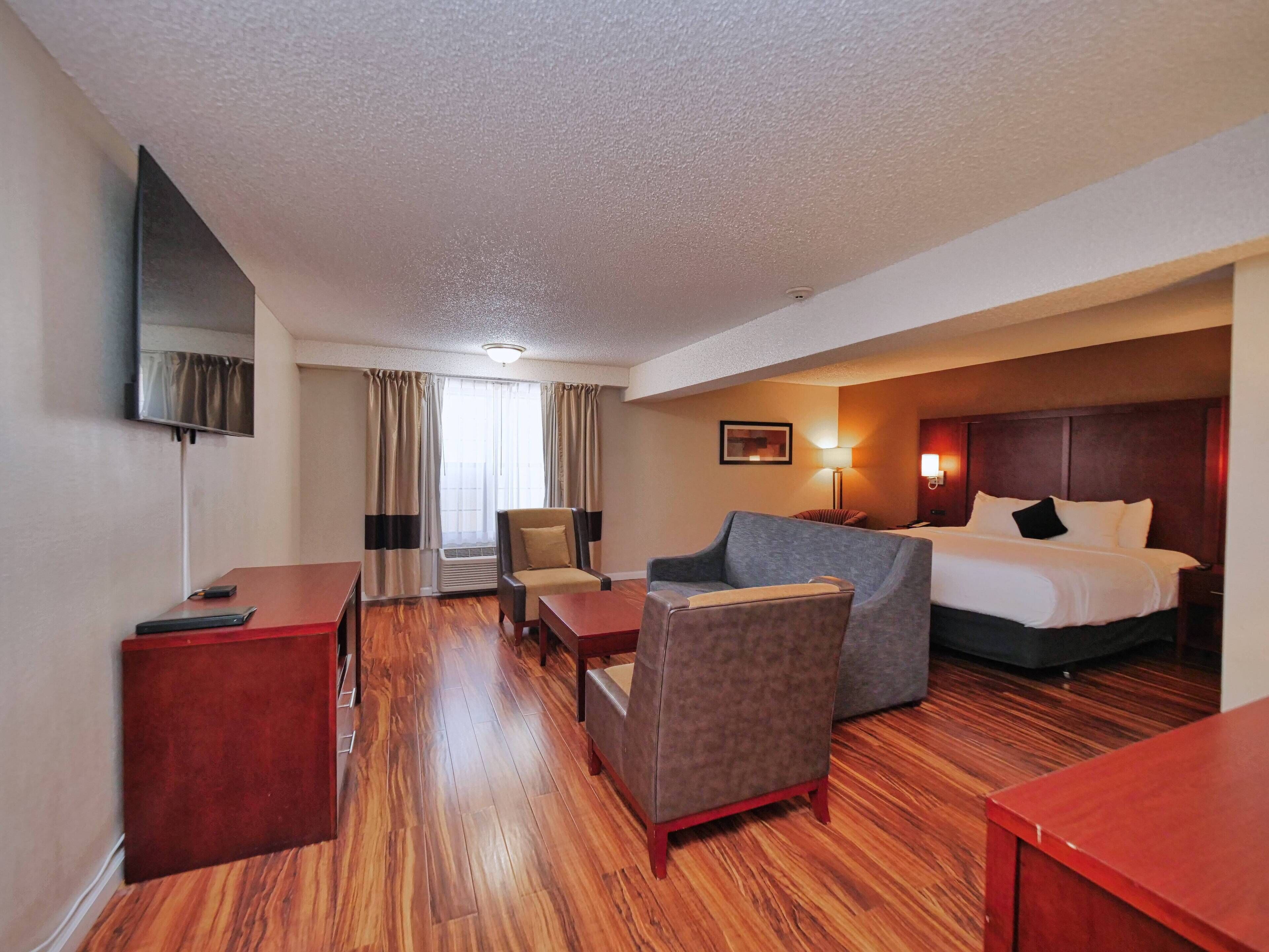 A hotel room with a bed, a desk, a chair, a sofa, and a TV mounted on the wall.