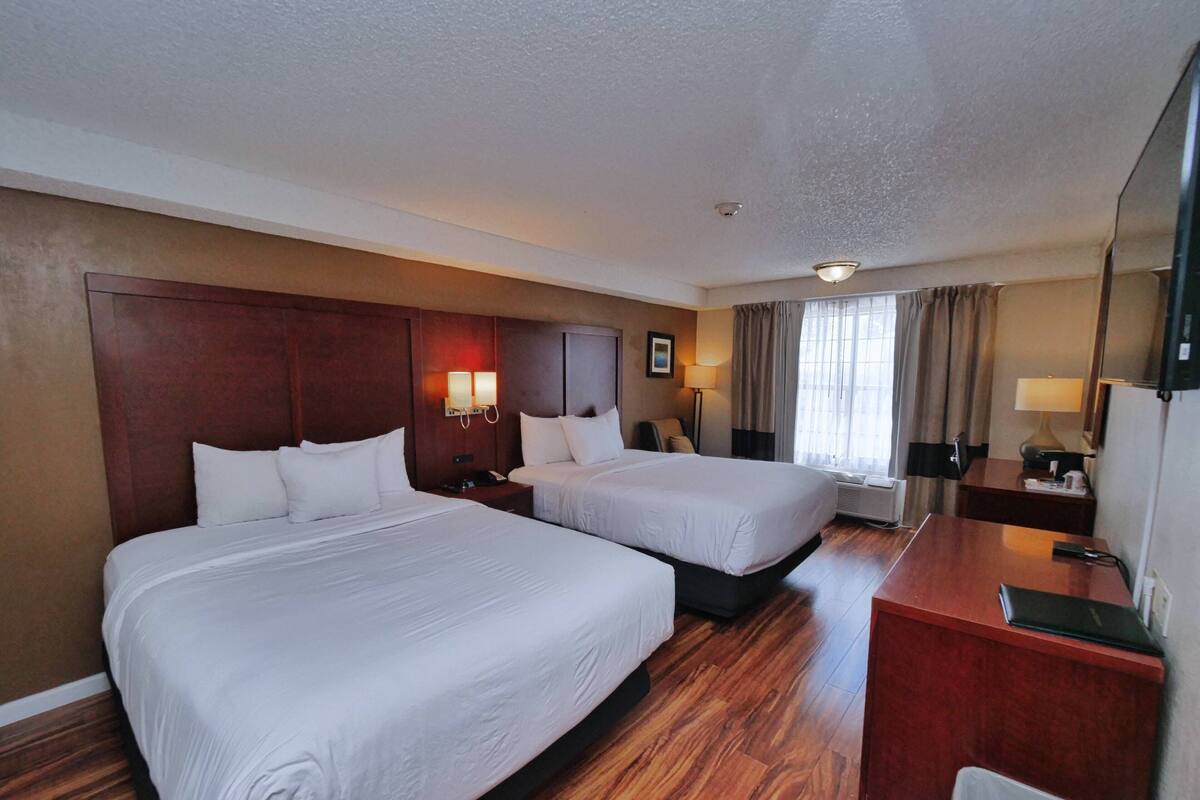 Habitación de hotel con dos camas, un escritorio, una silla, una lámpara, un televisor y una ventana con cortinas.