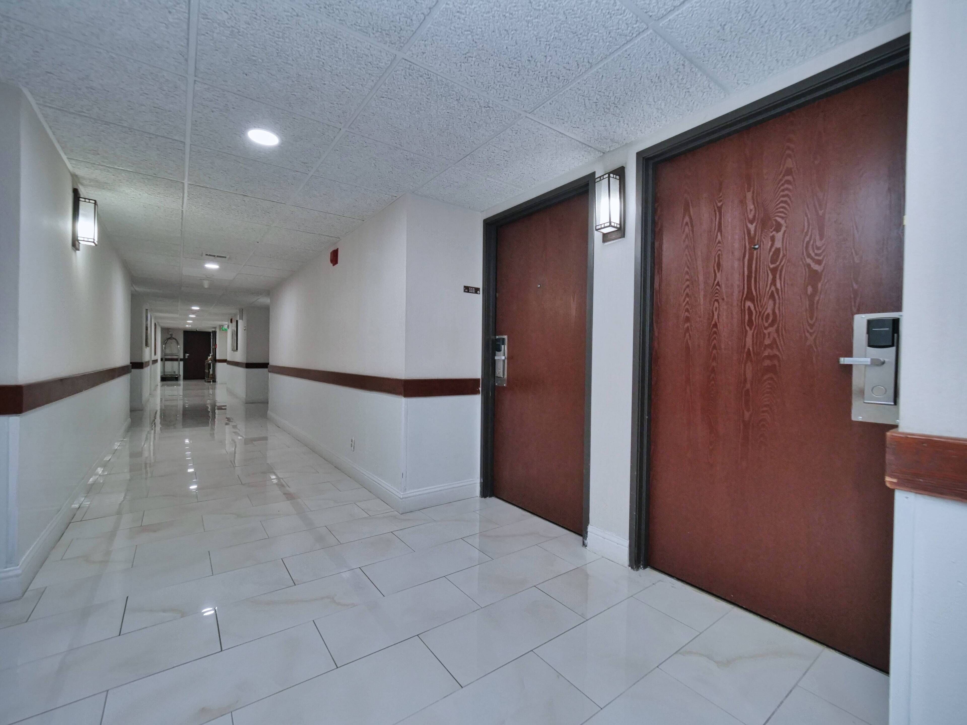A clean, well-lit hallway with white tiled floors and wooden doors.