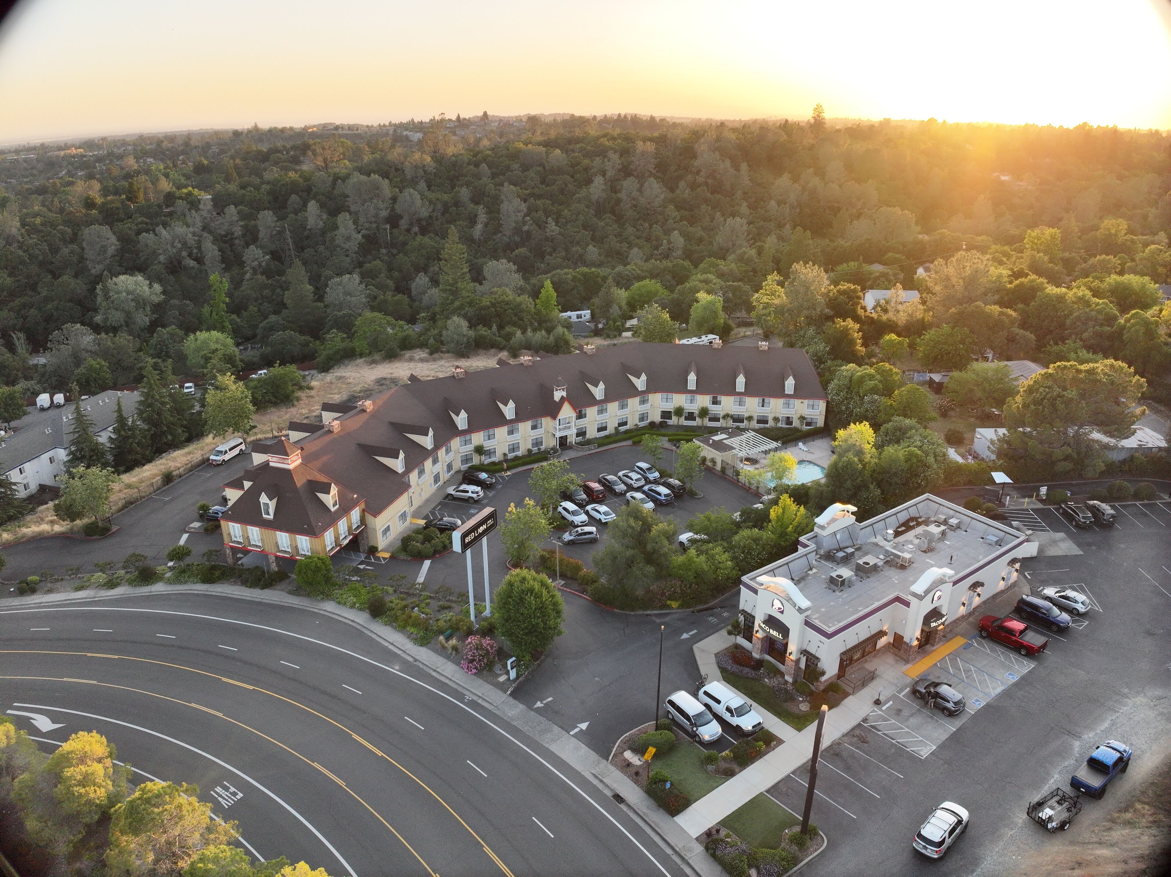 An aerial view of a hotel with a parking lot, a swimming pool, and a landscaped area.